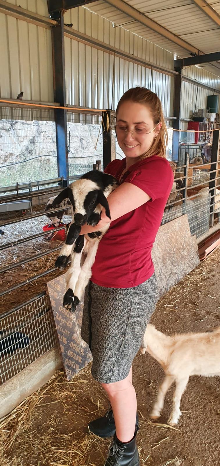 Tally holding a young goat in a barn, smiling down at it